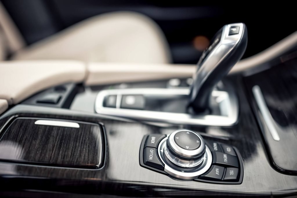 A shallow-depth-of-field close-up of a premium vehicle's center console, featuring an ergonomic electronic gear selector, a multi-function rotary controller, and wood-grain trim, representing high-end transmission repair and luxury car maintenance.