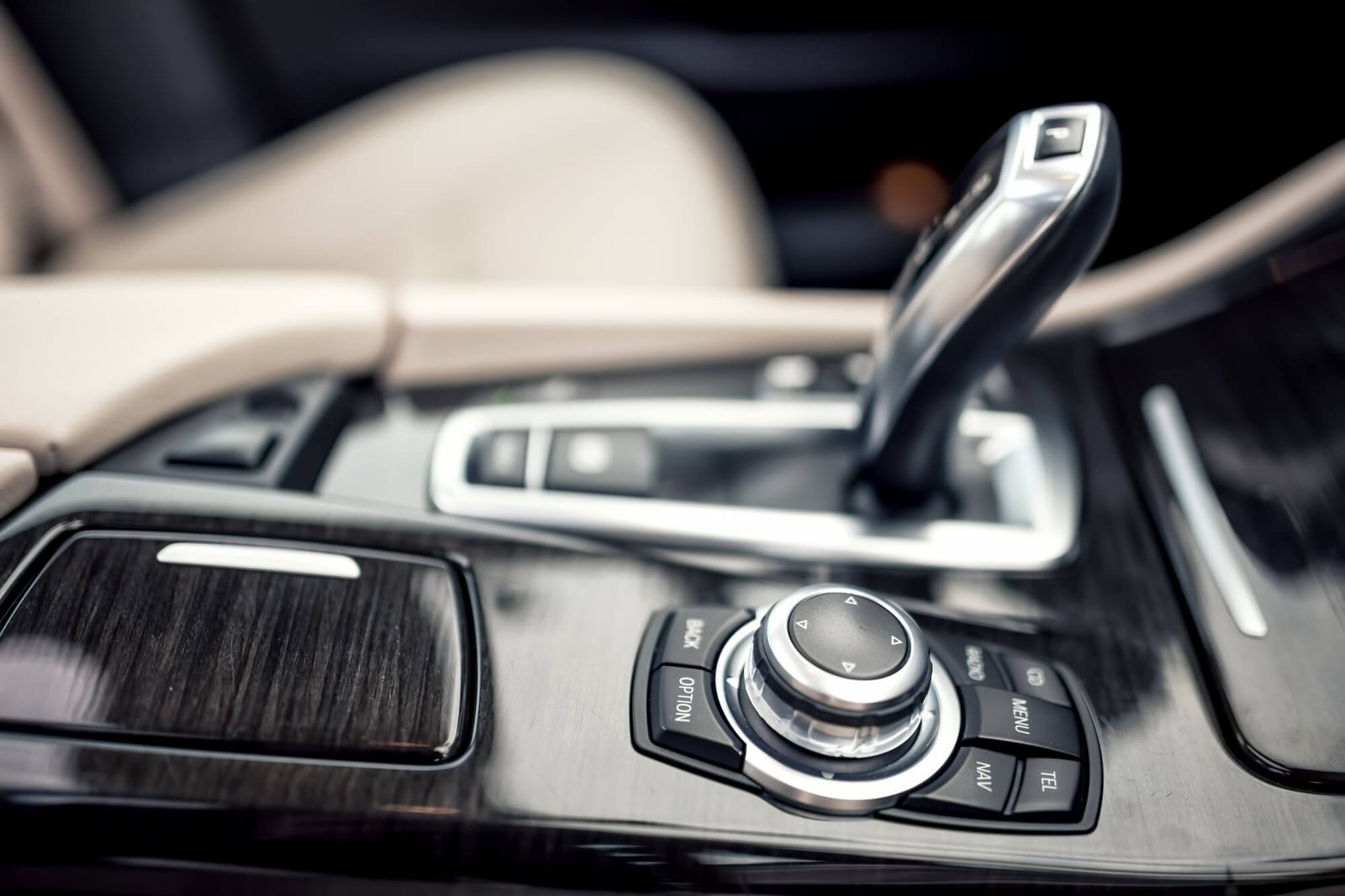 A shallow-depth-of-field close-up of a premium vehicle's center console, featuring an ergonomic electronic gear selector, a multi-function rotary controller, and wood-grain trim, representing high-end transmission repair and luxury car maintenance.