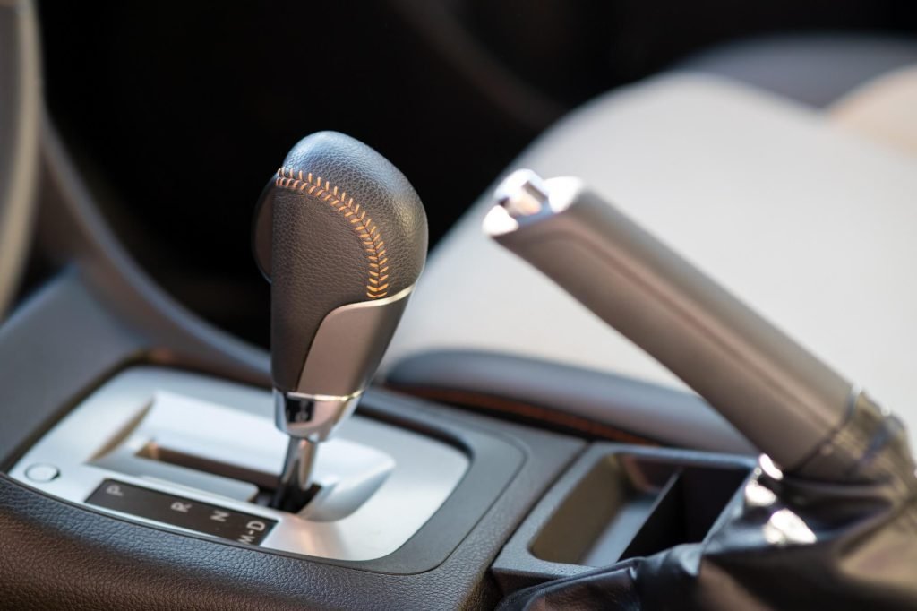 A close-up, high-detail photograph of a modern car's center console, featuring a leather-wrapped automatic gear shifter with orange contrast stitching.