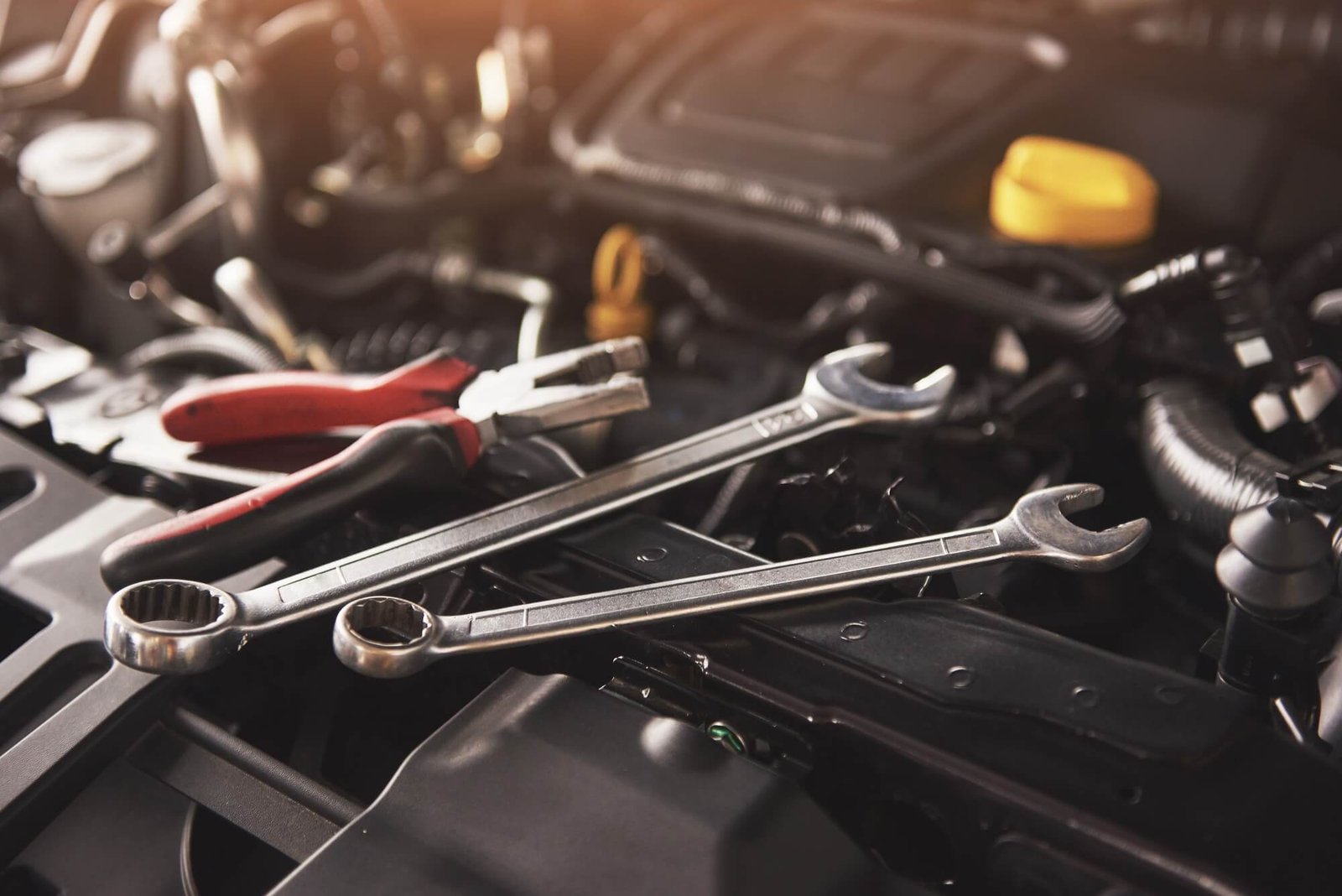 Professional mechanic's wrenches and pliers resting on a modern car engine