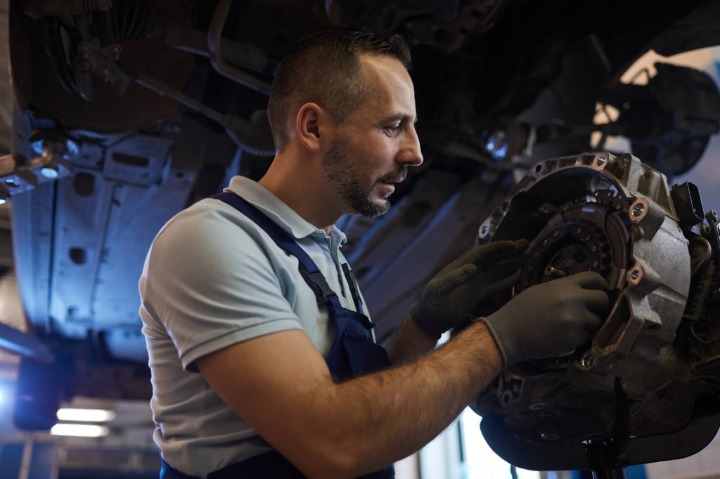 A skilled specialist performing a precise transmission repair on a vehicle's bell housing and clutch assembly while it is mounted on a shop lift.