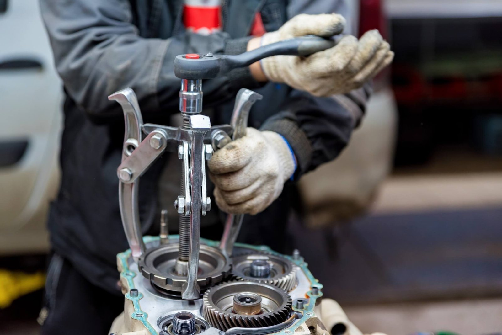A skilled specialist using a heavy-duty three-jaw bearing puller to remove a gear or bearing from a transmission case